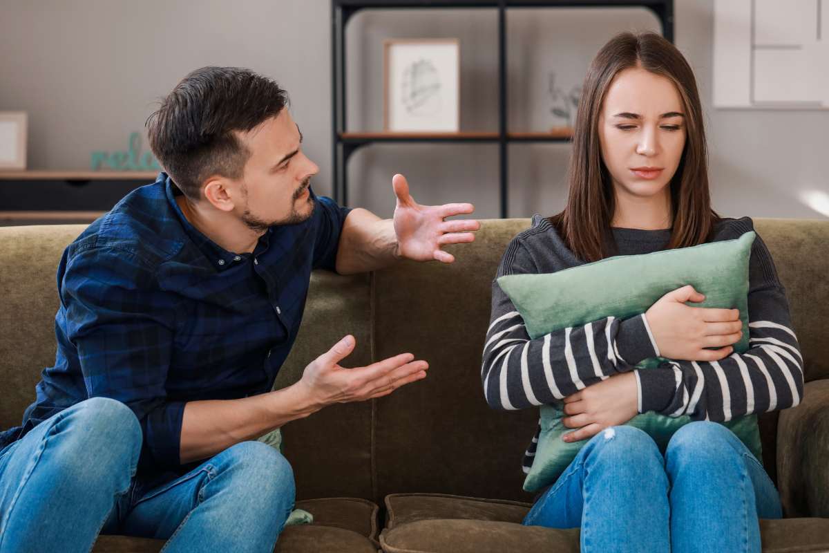 marito e moglie discutono seduti su divano lei si copre con cuscino