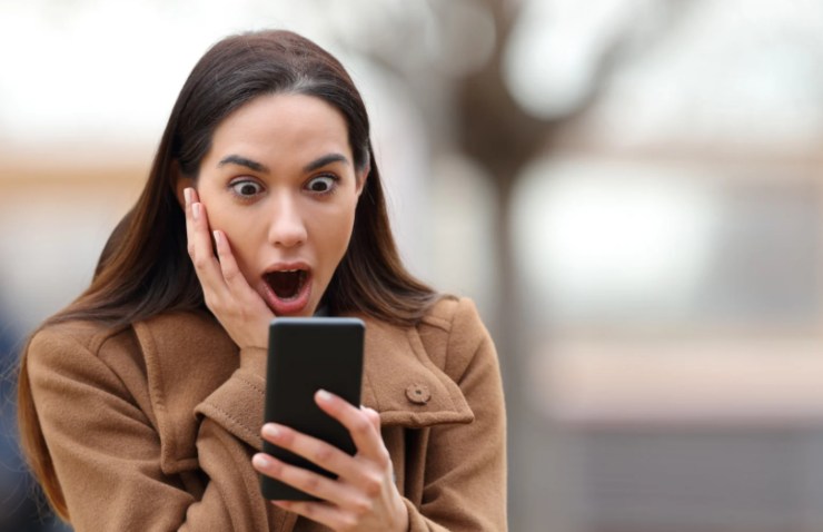 donna scioccata a bocca aperta mentre guarda il cellulare