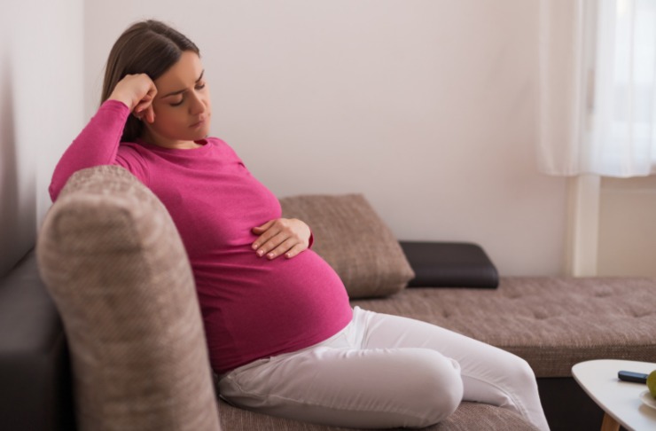 donna incinta triste seduta sul divano che si tocca il pancione