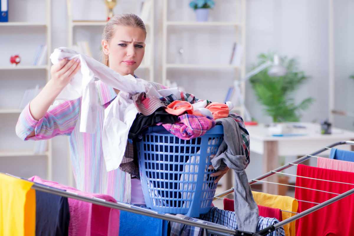 Donna con panni nel cesto che guarda maglietta preoccupata
