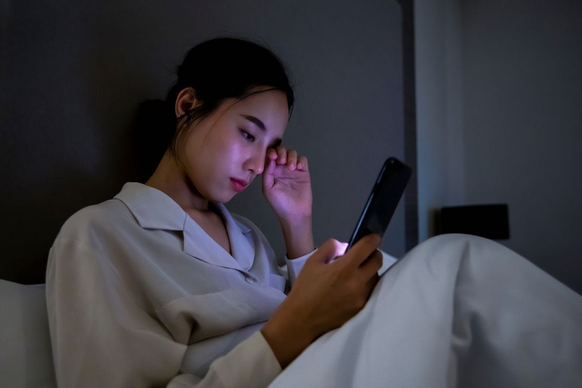 Donna con cellulare in mano sul letto
